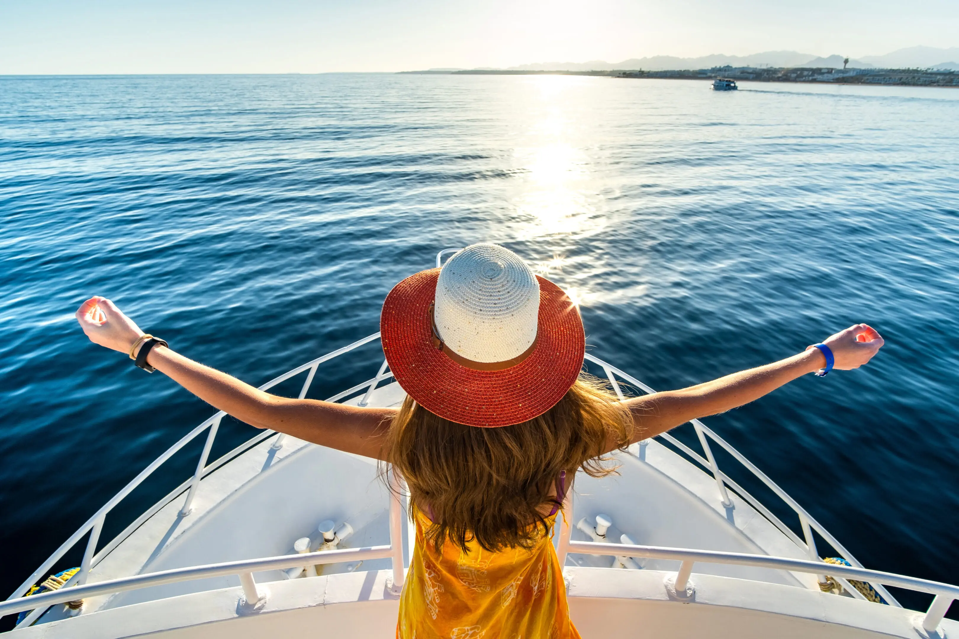 A woman in a red hat enjoys the ocean view from a boat.