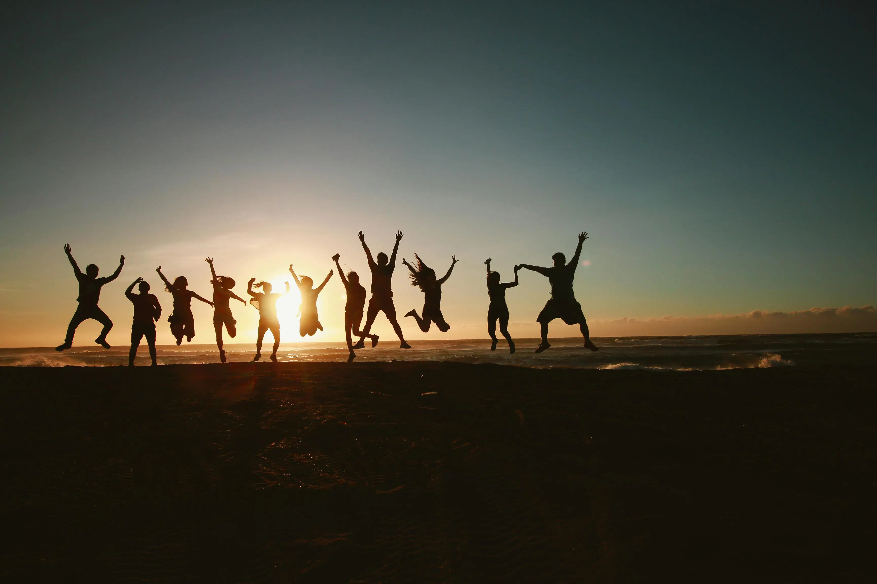 Group of friends jumping joyfully on the beach at sunset.