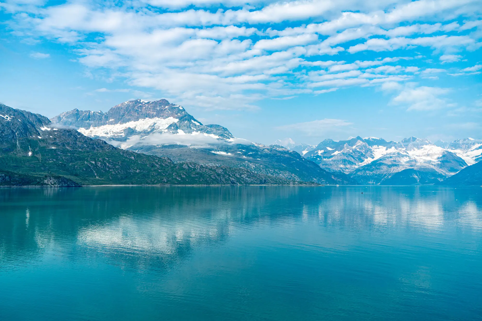 Serene lake reflecting snow-capped mountains under a partly cloudy sky.
