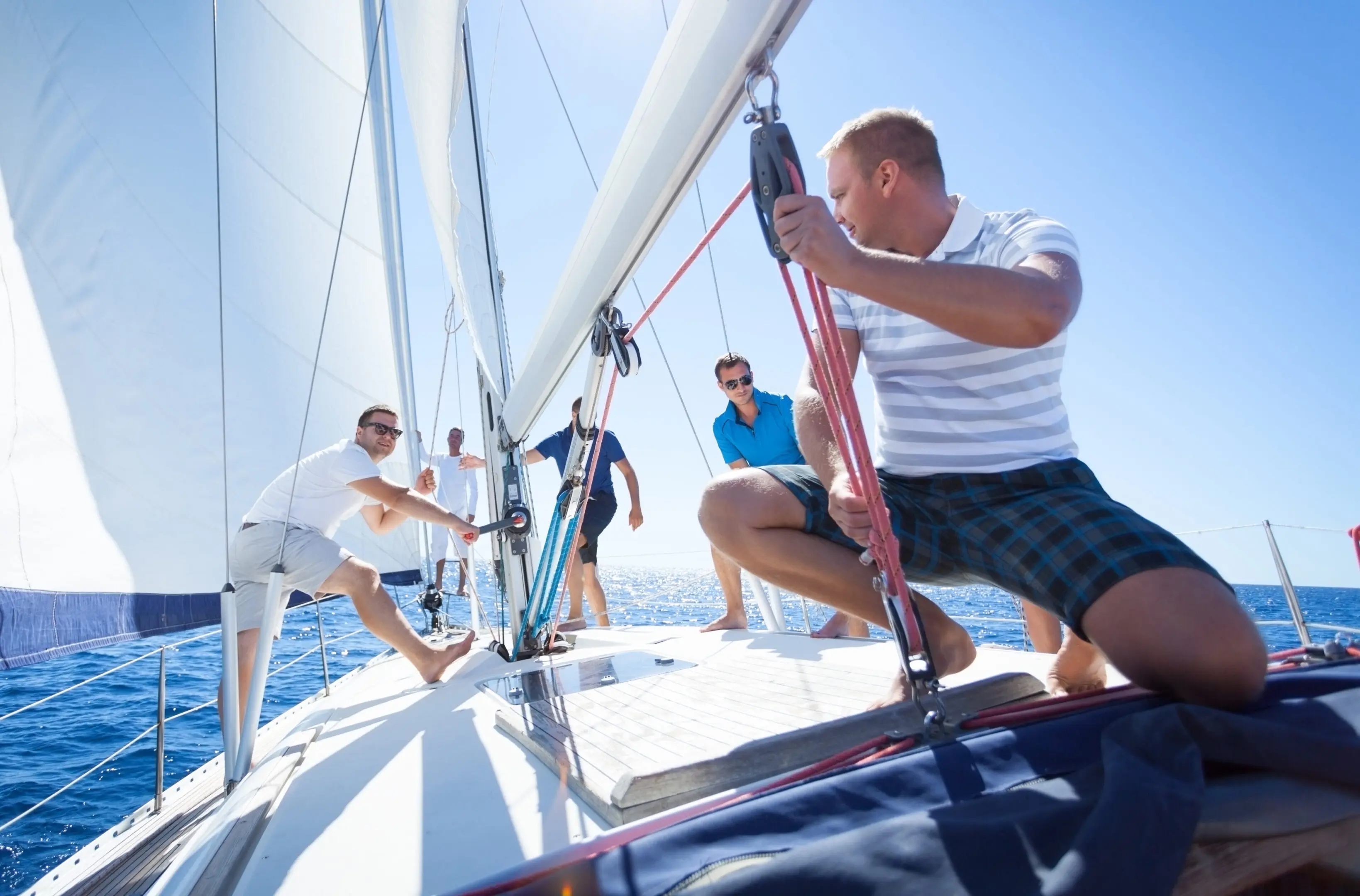 Four men working together on a sailboat under clear skies.