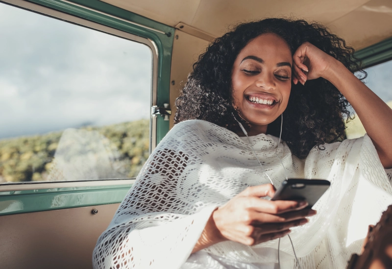 A woman smiling while looking at her phone inside a vehicle.