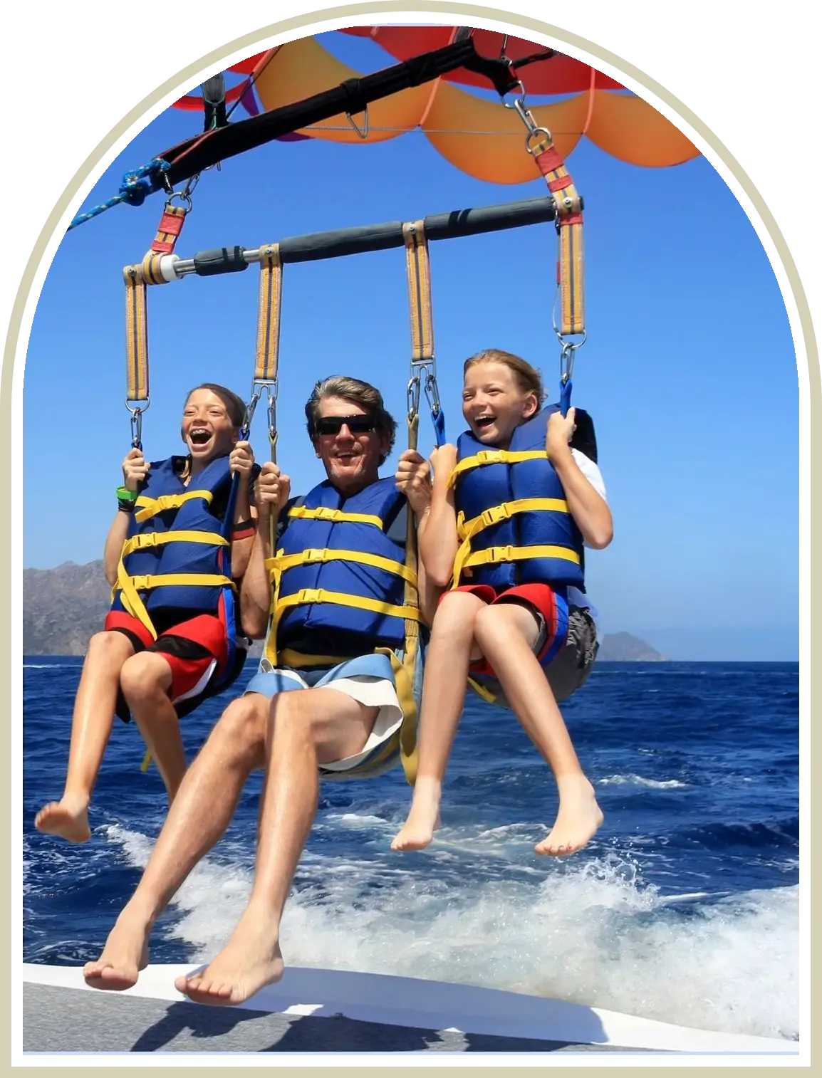Three women parasailing over the ocean, wearing life jackets and smiling.