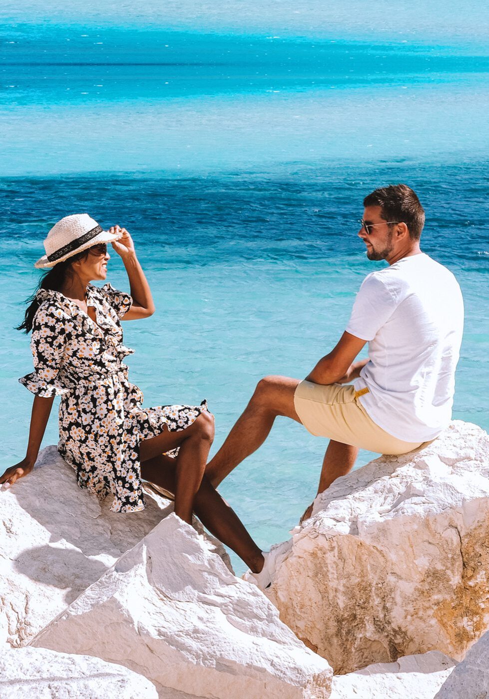 Couple enjoying a sunny day by the blue ocean on white rocks.